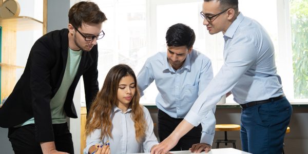 Mentor explaining marketing data interns. Confident office worker showing diagram to three pensive and focused colleagues. Mentorship concept